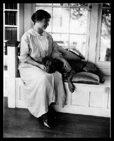 an old photo of a woman sitting on a window sill with a dog in her lap