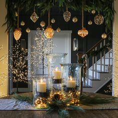 candles are lit in glass vases on a table with greenery and christmas lights