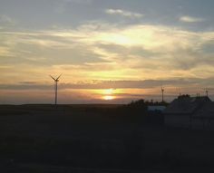 the sun is setting behind some windmills in an open field with houses and trees