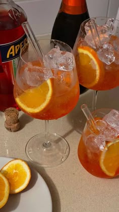 three glasses filled with orange juice and ice on a table next to two bottles of soda