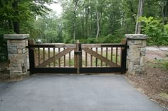 a wooden gate with stone pillars is open to the road in front of some trees