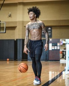 a man with tattoos is playing basketball in an indoor gym while looking at the ball