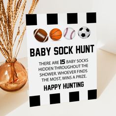 a baby sock hunt sign sitting on top of a table next to a vase filled with dry grass