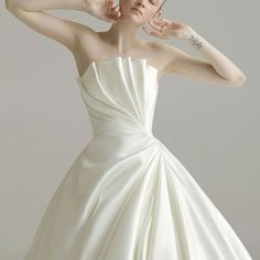 a woman in a white dress posing for the camera with her hand on her head