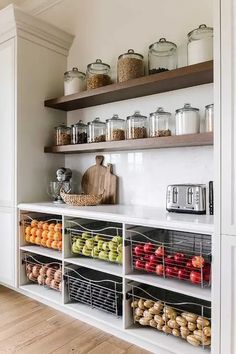 an organized kitchen with open shelving and lots of food on the counter top, including apples