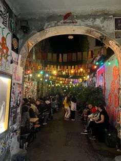 a group of people are sitting in an alleyway with lights hanging from the ceiling