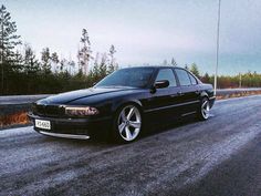 a black car parked on the side of a road in front of some pine trees