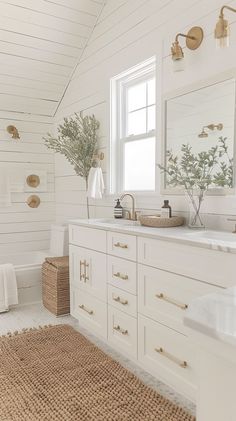 a bathroom with white walls and wood flooring, gold hardware on the vanity mirror