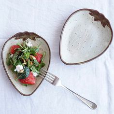 two heart shaped dishes with strawberries and spinach on them, one has a fork in it