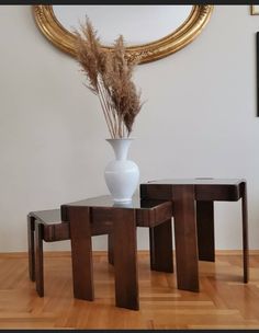 a white vase sitting on top of a wooden table next to two small stools