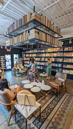 people are sitting in chairs and reading books at the library with lots of bookshelves