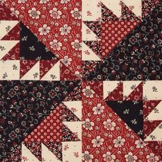 a red and black patchwork quilt with white flowers on the bottom, one block has an arrow in it