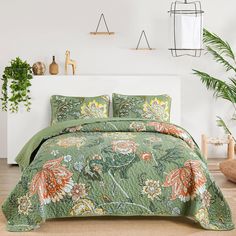 a bed with green bedspread and pillows in a room next to a potted plant