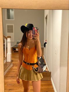 a woman taking a selfie in front of a mirror wearing a cowboy hat and skirt