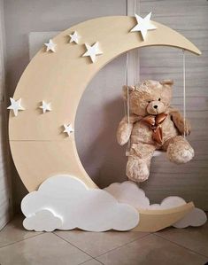 a teddy bear sitting on top of a crescent shaped moon with stars hanging from it