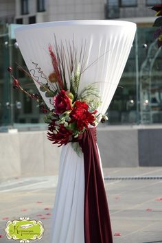 a flower arrangement on top of a white table cloth draped with red and green flowers