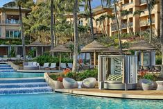 an outdoor swimming pool with lounge chairs and umbrellas next to the resort's main building