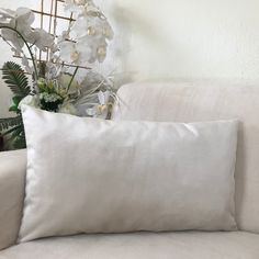 two white pillows sitting on top of a couch next to a vase filled with flowers