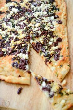 a pizza with olives, cheese and other toppings on a wooden cutting board