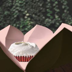 a cupcake in a pink heart shaped box on a table with trees in the background