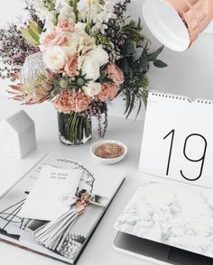 a table with flowers and calendars on it, including an alarm clock next to the desk