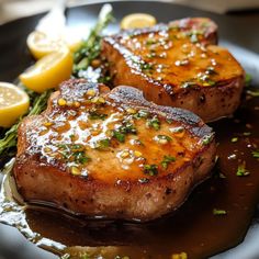 two pieces of meat sitting on top of a plate with lemons and parsley