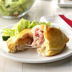 a white plate topped with a pastry filled with meat and veggies next to a salad