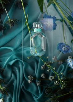 a bottle of perfume sitting on top of a blue cloth next to flowers and leaves