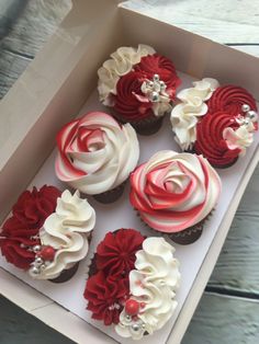 cupcakes with red and white frosting in a box on a wooden table