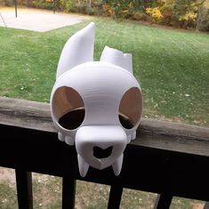 a paper mache mask on the side of a wooden fence with grass in the background