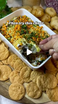 a person dipping some food into a bowl on top of a wooden platter with crackers