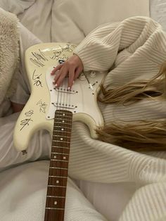 a person laying in bed with a guitar on their lap and writing on the strings