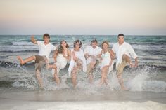 a group of people jumping into the water at the beach with their feet in the air