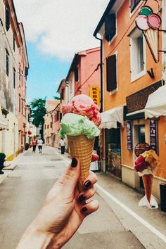 a hand holding up an ice cream cone in front of some buildings on a street