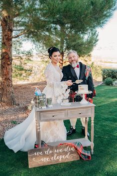 a bride and groom cutting their wedding cake at the end of an outdoor ceremony in front of a pine tree