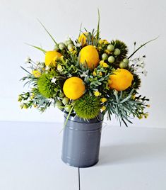 an arrangement of oranges and greenery in a gray bucket on a white surface