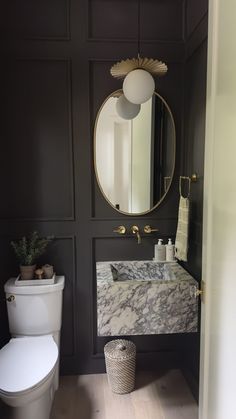 a white toilet sitting next to a bathroom sink under a round mirror on a wall