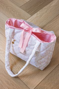 Fantasy Tote Bag in an exclusive watercolor castle and rose pattern. Quilted and lined in white, with a pink ribbon bow closure. It features a gold heart zipper pull and a front pocket. The interior has pockets and is lined in pink and says "Made of magic". It has long shoulder straps. 11.5" x 9.5" / 22" strap *Final sale / not eligible for discounts Ribbon Tote Bag, Sew Tote Bag, Watercolor Castle, Bow Tote Bag, Pink Tote Bag, Work Tote Bag, Tote Bags Sewing, Quilted Tote Bags, Pink Tote Bags