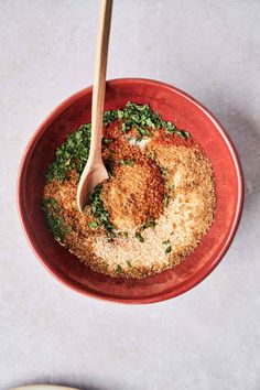 a red bowl filled with food on top of a white table next to a wooden spoon