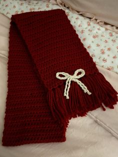 a red knitted scarf with a white bow on it sitting on a bed next to a pillow