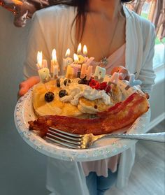 a woman holding a plate with bacon and candles on it