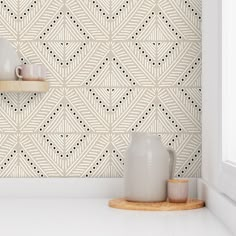 two white vases sitting on top of a counter next to a wall with geometric designs