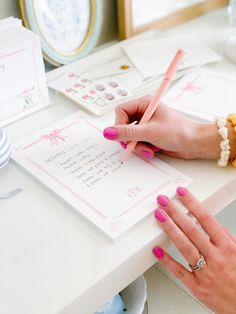 a woman's hands with pink nail polish writing on a note