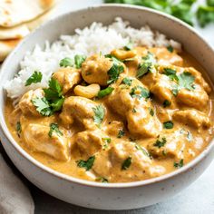 a white bowl filled with chicken curry and rice on top of a table next to pita bread