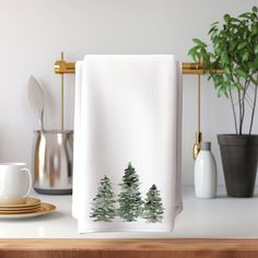 a white towel with trees on it sitting on a counter next to a cup and saucer