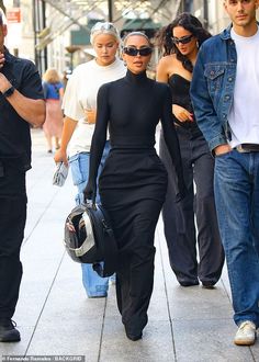 three people walking down the street with one carrying a motorcycle helmet in her hand and wearing sunglasses