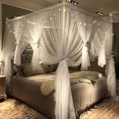 a canopy bed with white curtains and lights on the headboard is in a bedroom