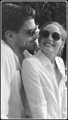 a black and white photo of a man and woman kissing in front of some trees