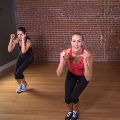 two women doing squats in front of a brick wall with one holding her hands up