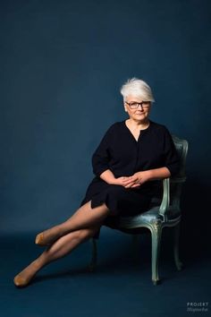 an older woman with white hair sitting on a chair in front of a blue background